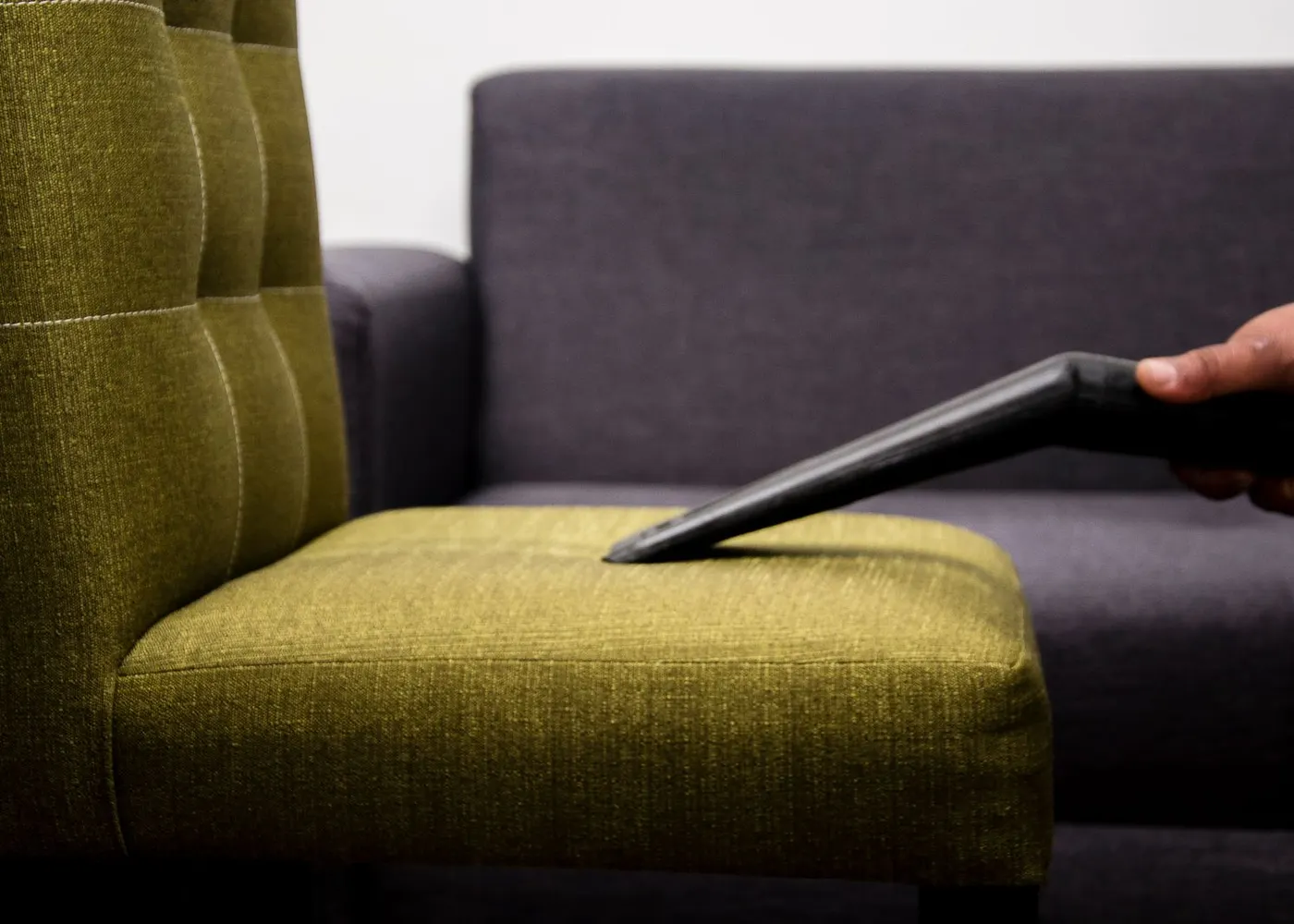 A person vacuuming an upholstered chair